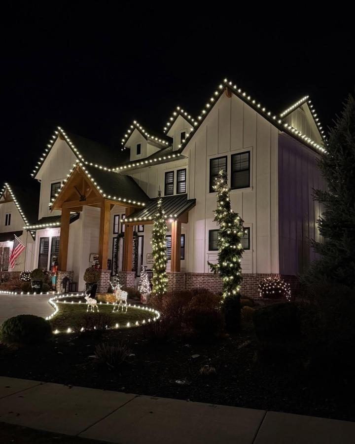 A modern farmhouse with every roofline and porch post wrapped in lights, and stake lights along the walkway